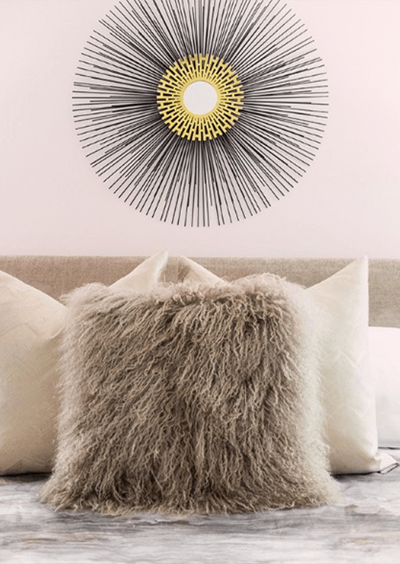 A close-up of a bed with accent pillows and modern art hung above on a pale pink wall.