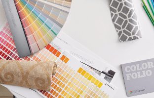 A table covered with color swatches, fan decks, fabric and colored pencils.