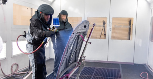 two people in paint booth spraying car hood