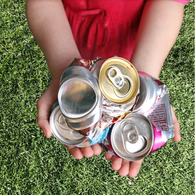child holding crushed beverage cans standing on green grass