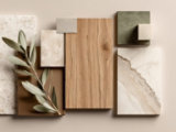Flat lay of mixed materials: wood, marble, tiles, fabric, stone sphere, and green leaves.