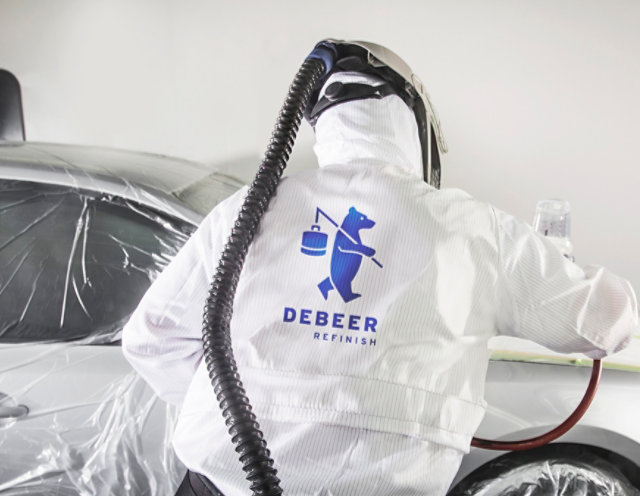 Automotive coatings being spray gun applied by a person wearing Debeer overalls