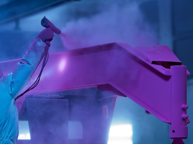 Technician applying OneCure™ powder coating in an industrial finishing facility.