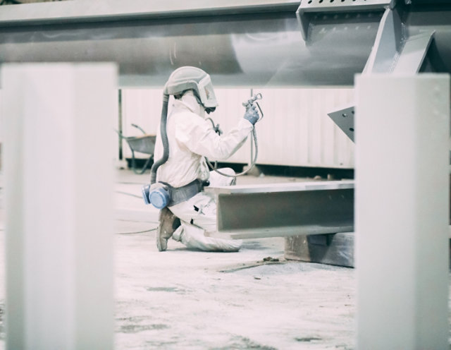 Applicator spraying fire protective coating on steel beam in a shop