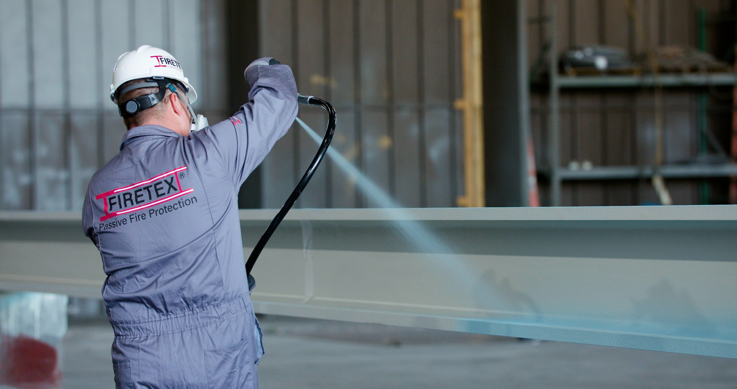 person spraying fire protection coating onto steel beam