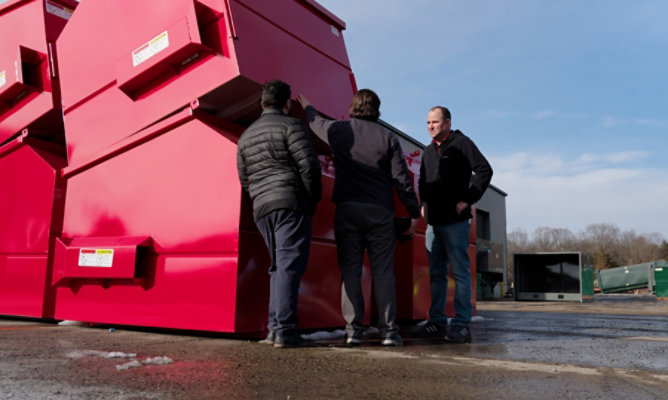 Inspecting large red industrial waste containers at a manufacturing facility