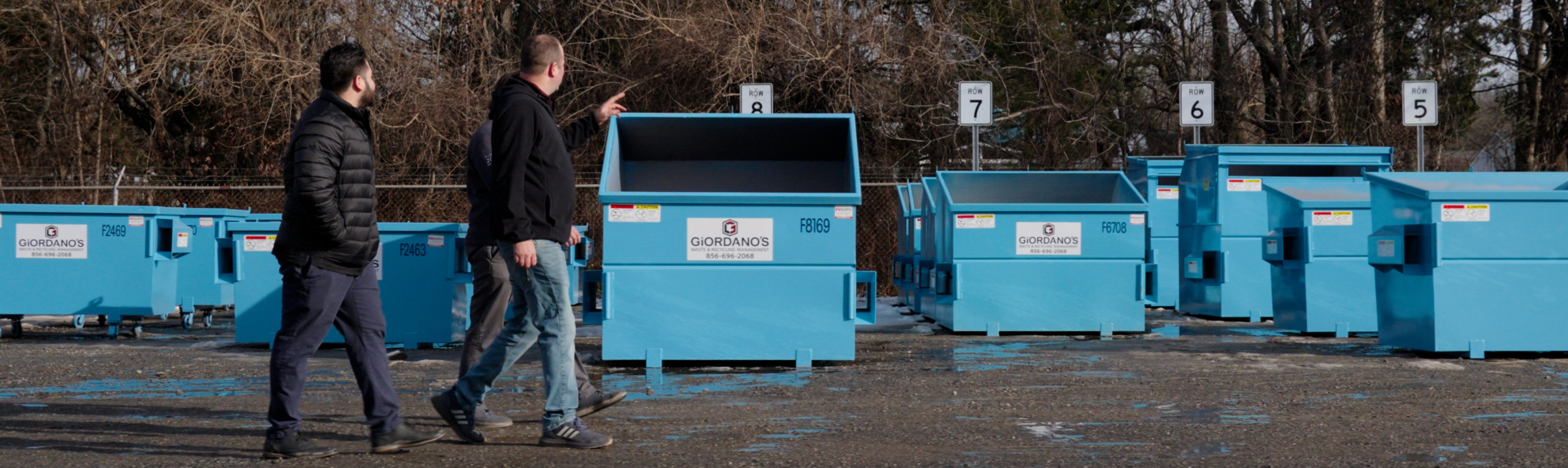blue dumpsters in background as two people walk by