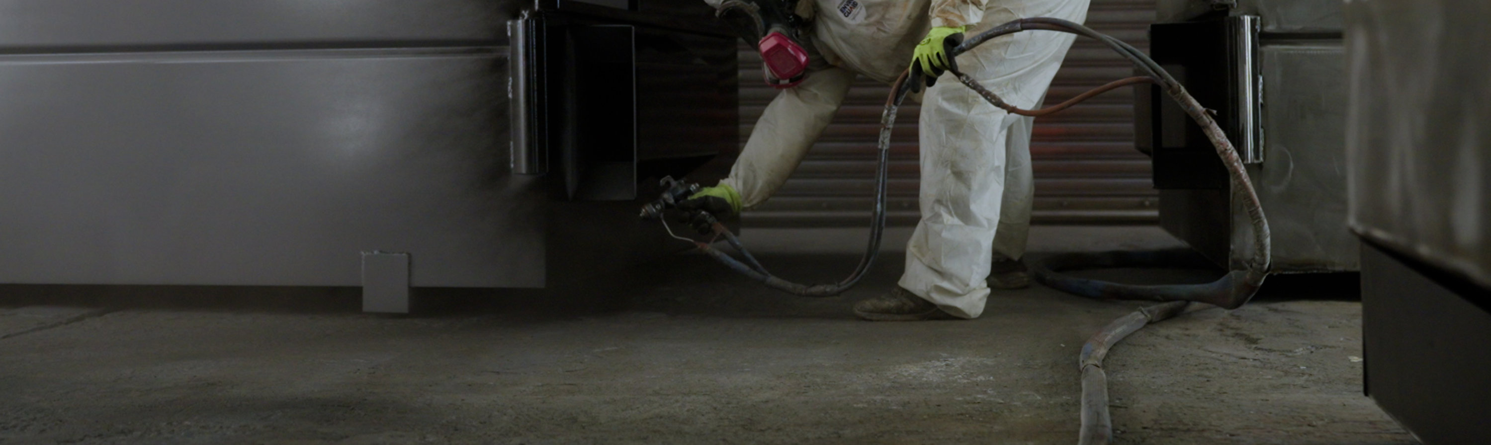 person applying coating with spray to a dumpster