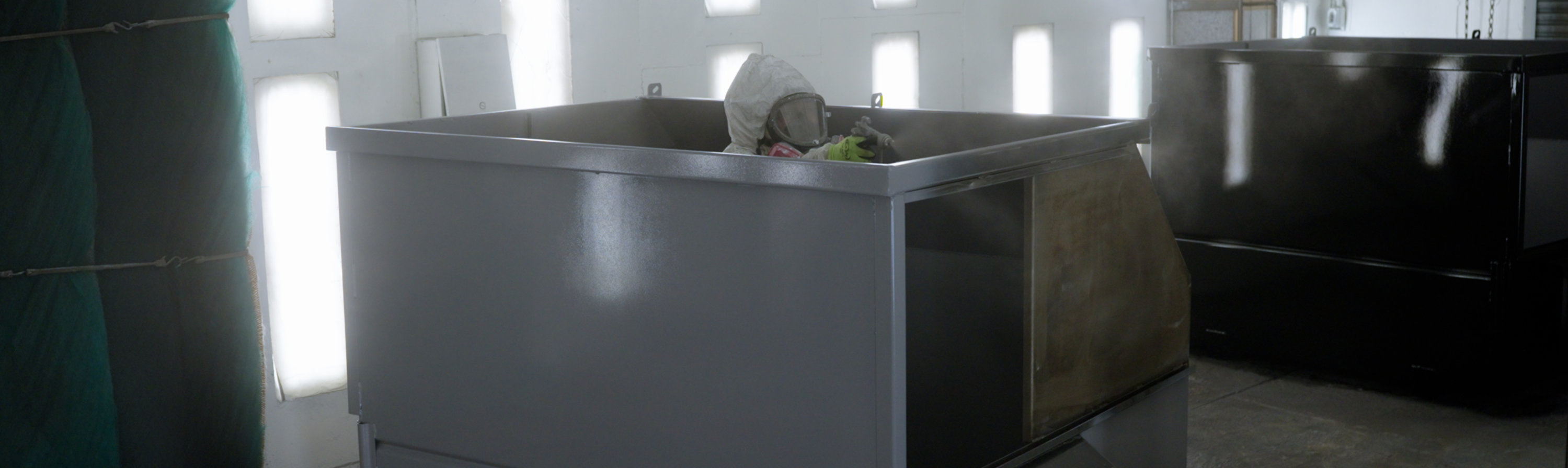 painter applies coating to dumpster from inside the dumpster