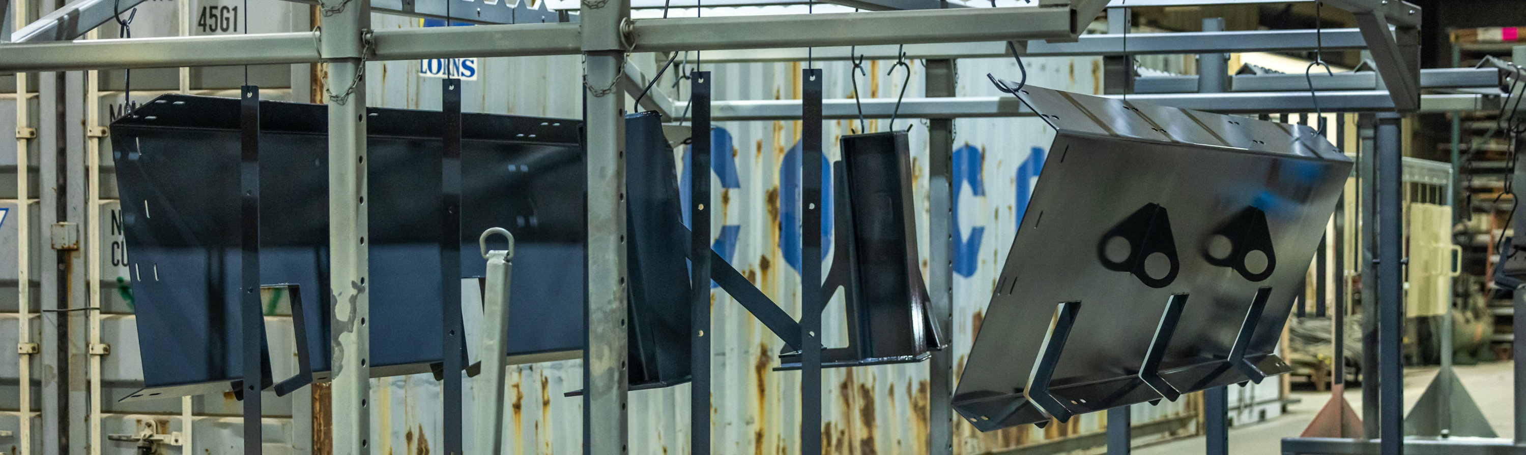 Large black powder-coated metal components hang from a wheeled production rack inside a manufacturing facility.