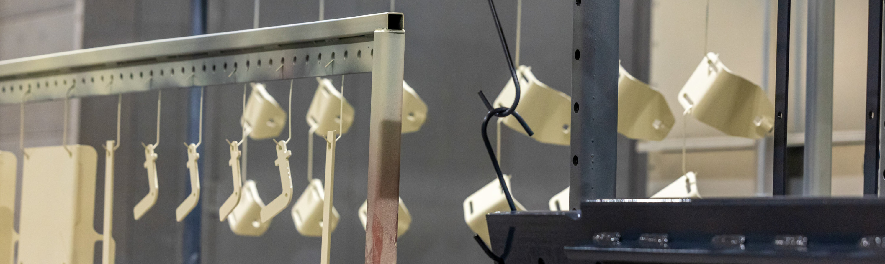 Various light-colored and black metal components hang from industrial racks inside a powder-coating facility. 