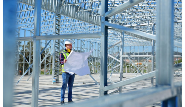A contractor looking over blueprints inside of the steel frame of a building