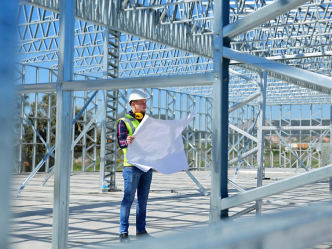 A contractor looking over blueprints inside of the steel frame of a building