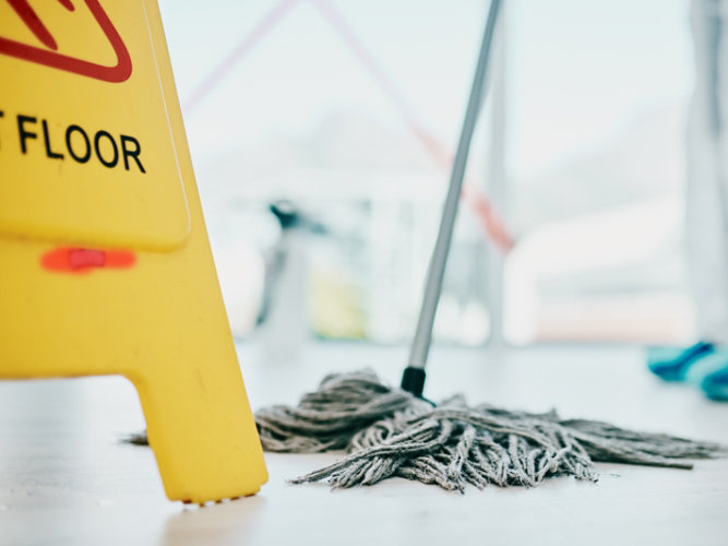 custodian mopping floor with yellow caution sign