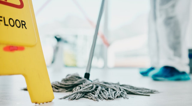 custodian mopping floor with yellow caution sign