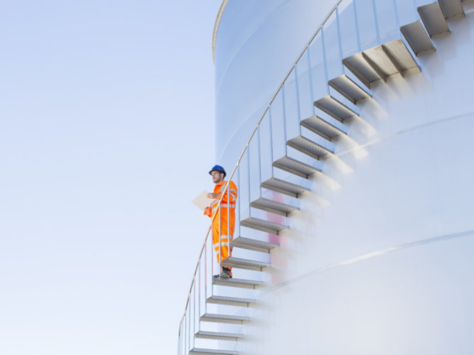 Man standing on steps outside of a oil and gas tank