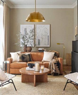 Pottery Barn living room painted in Urban Putty  SW 7532, with two white chairs facing a round wooden coffee table and brown couch with pillows, two neutral paintings, minimal decor, and gold light fixture.