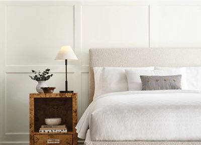 Bedroom with wainscoting painted Sherwin-Williams White Snow SW9541 with a white bed and wooden nightstand.