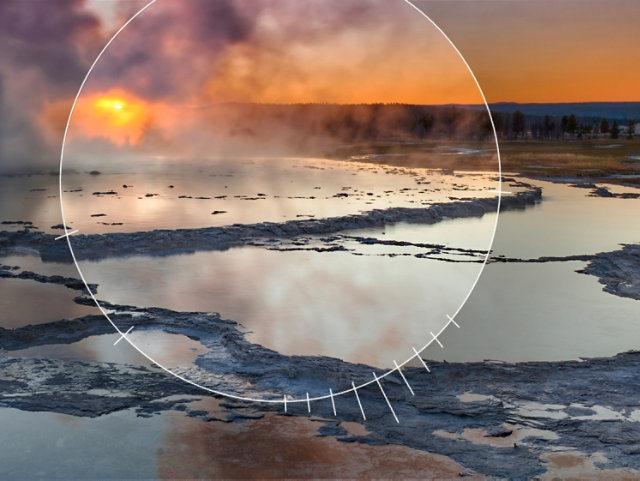 Photo of an erupting geyser surrounded by a pool of water with a sun setting in the background and an aperature dial focused on the geyser pool