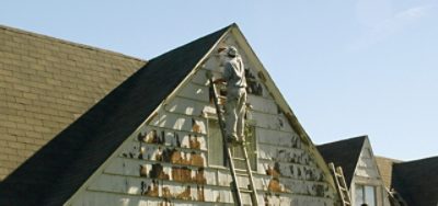 A man removing chipped paint from house