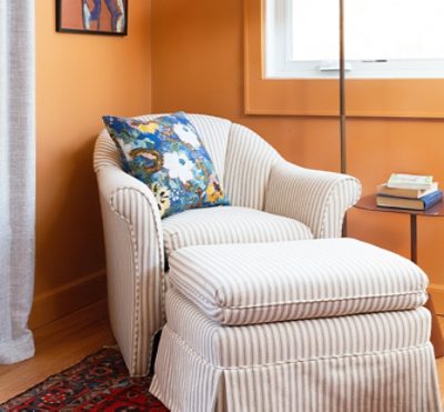 orange walls with a striped chair/ottoman near a window.