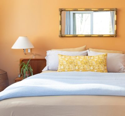 orange walled bedroom with a mirror above the bed and light at the side.