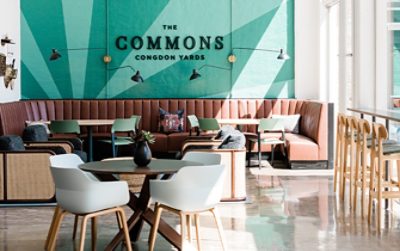 Image of the Commons Congdon Yards room with teal wall, brown leather seating near window.
