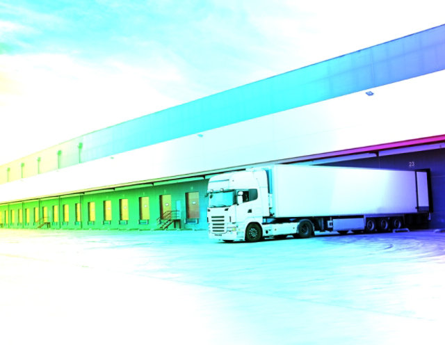 Red modern semi truck parked at the docks of a distributor, waiting to get loaded.