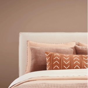 A bed with an ivory headboard and warm textiles against a wall painted Redend Point SW 9081.