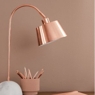 A shiny copper desk lamp in front of an interior wall painted Redend Point SW 9081.