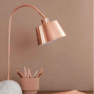 A shiny copper desk lamp in front of an interior wall painted Redend Point SW 9081.