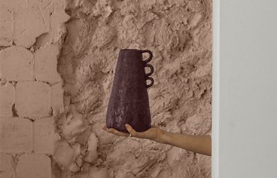 someone holding a piece of pottery in front of a textured clay like wall.