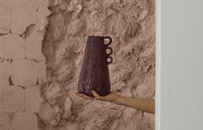 someone holding a piece of pottery in front of a textured clay like wall.