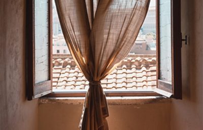 view looking out a window onto buildings with a tied up curtain.