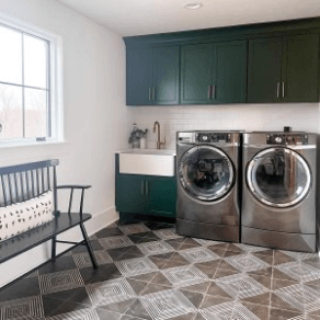 A bright, large laundry room with white painted walls and cabinets painted a forest green. 