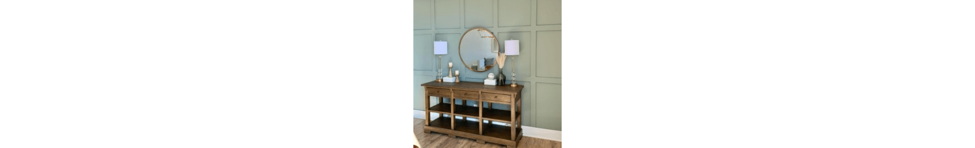 A console table stained a medium brown with lamps and décor on top against a wall painted a green-gray.