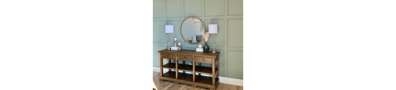 A console table stained a medium brown with lamps and décor on top against a wall painted a green-gray.