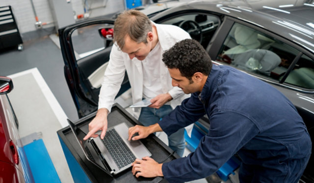Automotive technicians working together on a laptop.