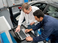 Automotive technicians working together on a laptop.