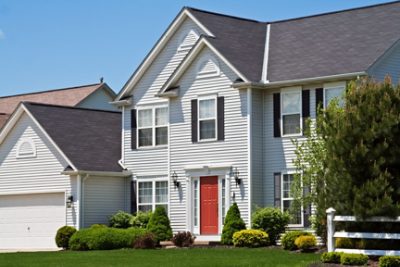 A large suburban home with neutral color vinyl siding and manicured landscaping.