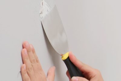 Paint Putty is being put on a wall with a putty knife.