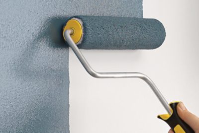 Gray blue paint being rolled onto a white wall with a paint roller. 