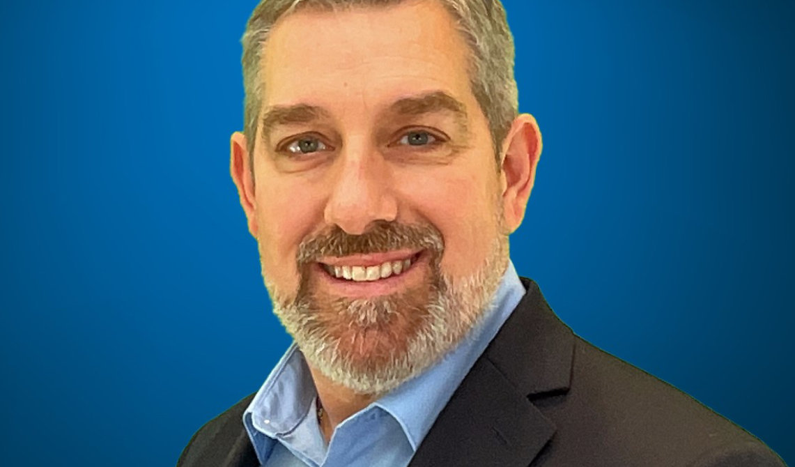 Headshot of Todd Hakenjos against a blue background.