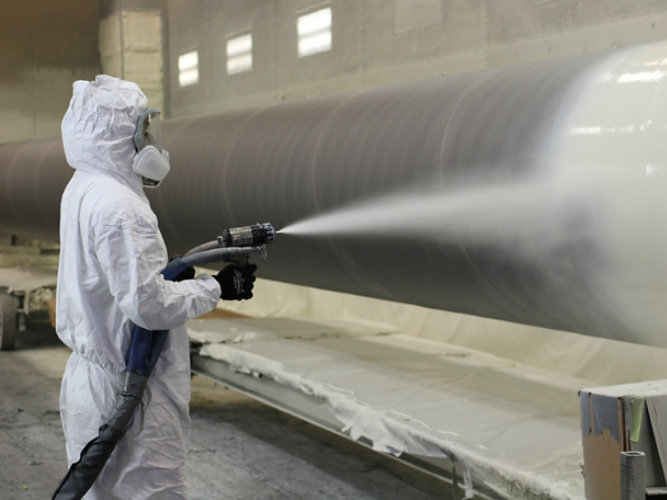 person spraying coating onto water transmission pipe