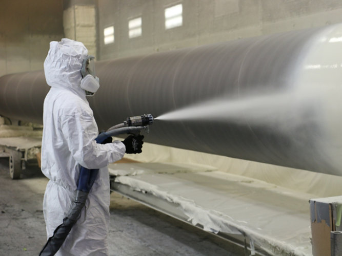 person spraying coating onto water transmission pipe