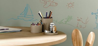 A small wooden desk with crayons and drawings on a blank wall. 