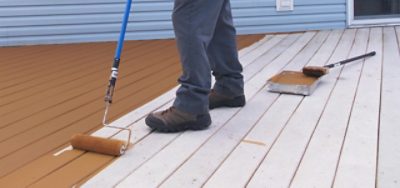 A person using a roller brush to paint a deck