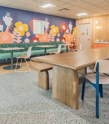 Ronald McDonald House dining area with a colorful floral mural, mint green banquettes, several small tables, and one large wooden table.