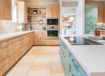 Spacious community kitchen in the Ronald McDonald House with wooden cabinets around the perimeter, accent and island cabinets painted Jasper Stone by Sherwin-Williams, new appliances, and pastel chevron backsplash.