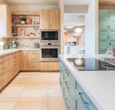 Spacious community kitchen in the Ronald McDonald House with wooden cabinets around the perimeter, accent and island cabinets painted Jasper Stone by Sherwin-Williams, new appliances, and pastel chevron backsplash.